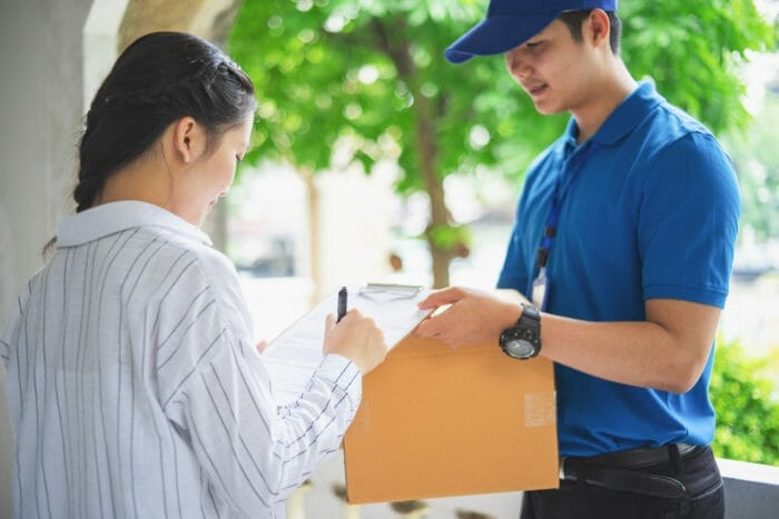 A woman signs to receive her green card from a mail delivery person.