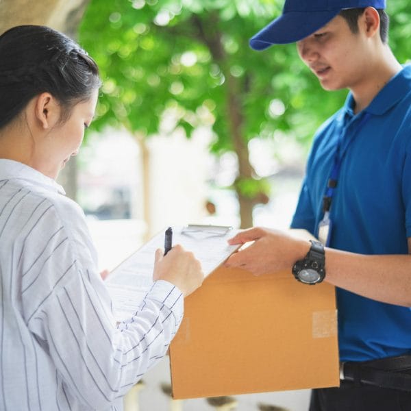 A woman signs to receive her green card from a mail delivery person.