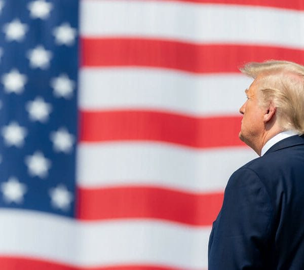 President Donald Trump stands in front of an American flag.