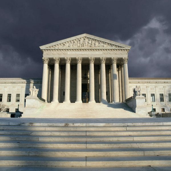 Straight-on view of the U.S. Supreme Court, somewhat lit in the foreground with ominous storm clouds gathering behind.